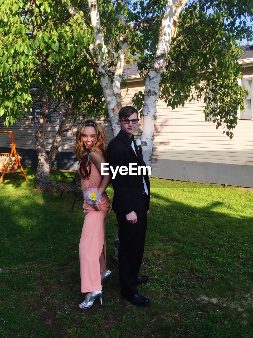 Full length of cheerful teenage couple standing on grassy field at yard during prom