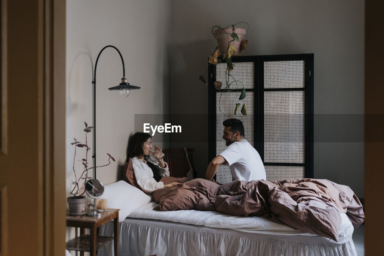 Couple talking to each other while sitting on bed at home