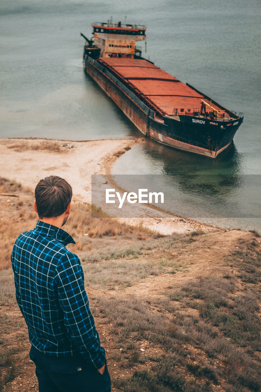 REAR VIEW OF MAN ON BOAT AT SHORE