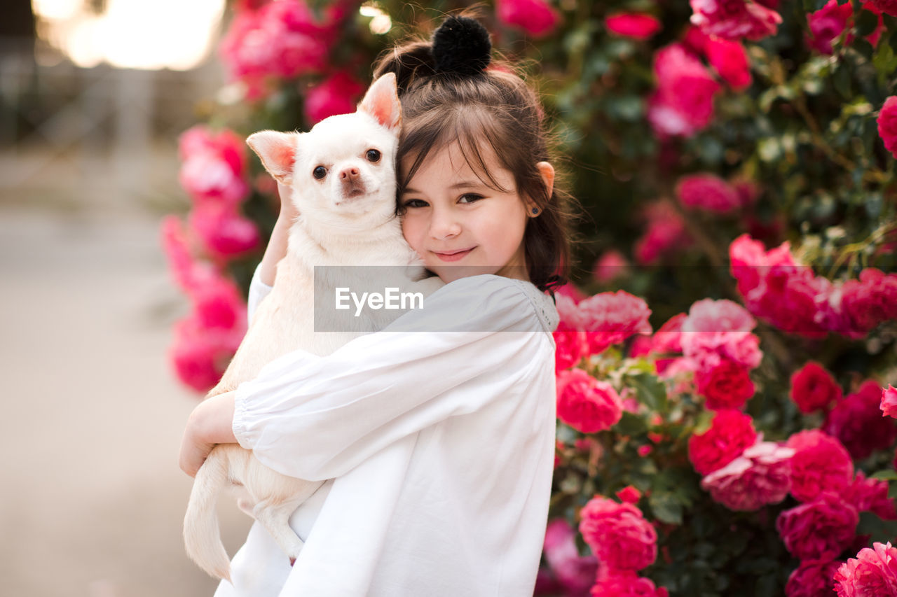 Pretty little child girl 4-5 year old hold chihuhua pet dog posing over flower background close up