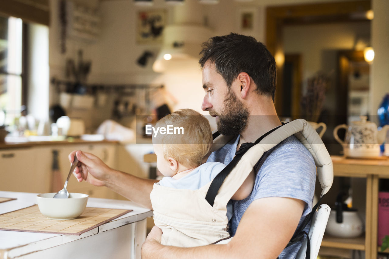 Father feeding baby in baby carrier