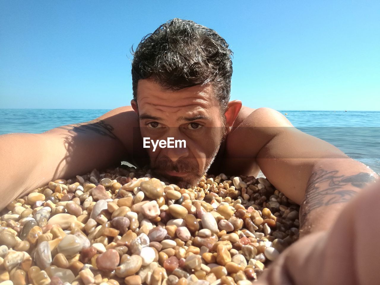 Close-up portrait of shirtless man lying at pebble beach