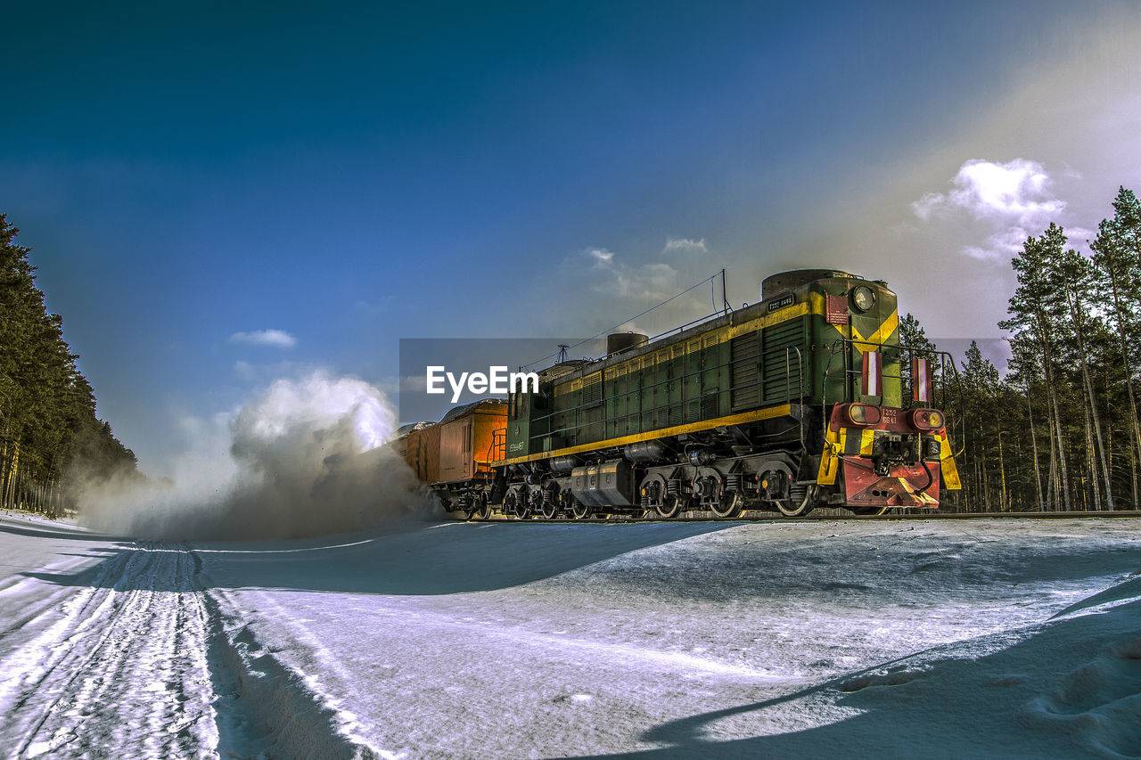 Train on railroad tracks by snowy field against sky