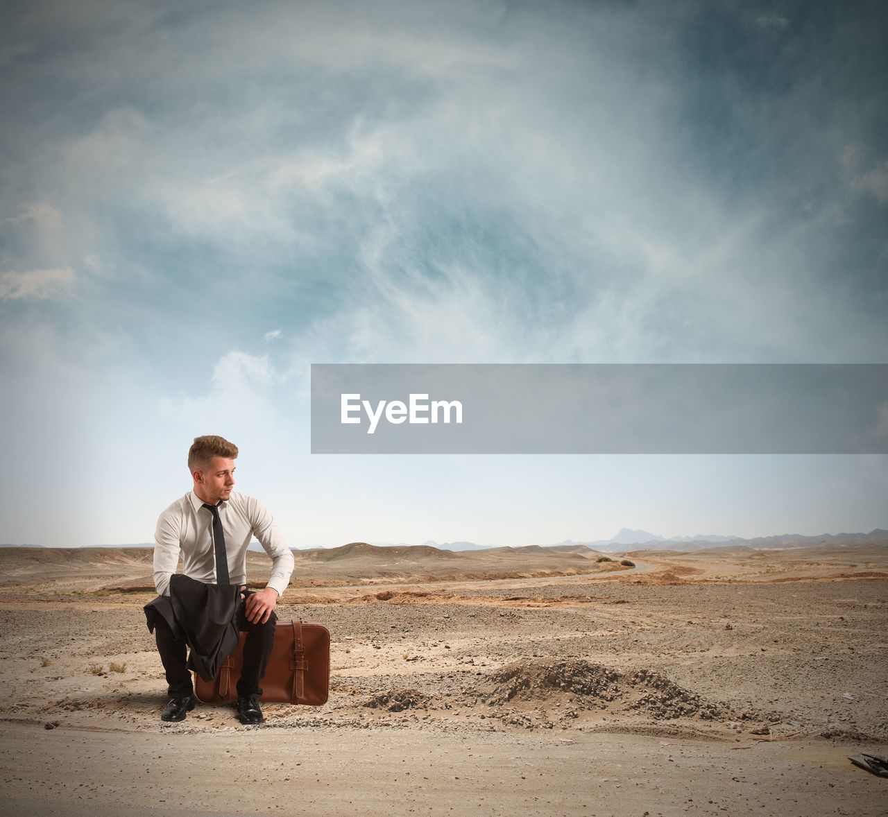 FULL LENGTH OF MAN SITTING ON LAND AGAINST SKY