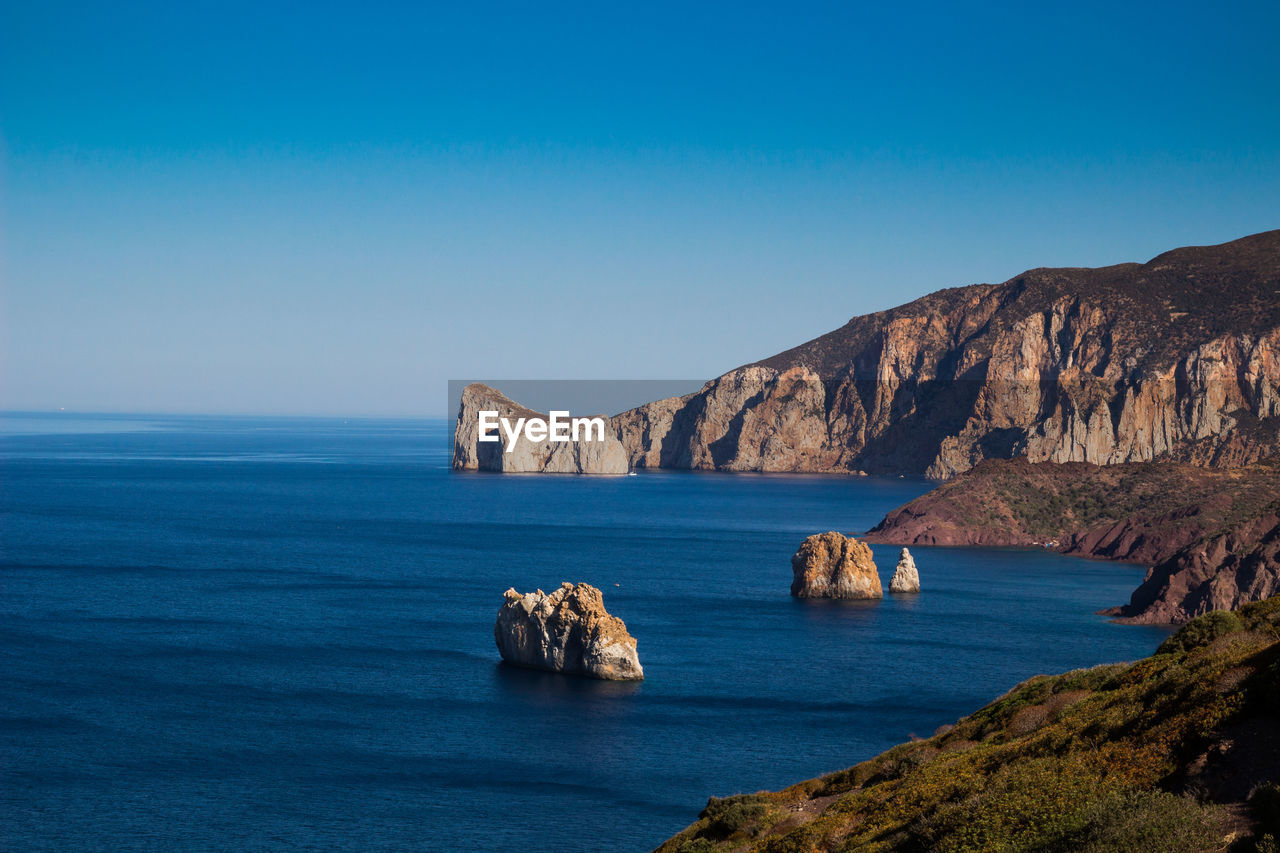 Scenic view of rocks in sea against clear blue sky