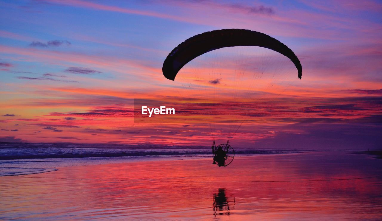 SILHOUETTE MAN FLYING OVER SEA AGAINST SKY