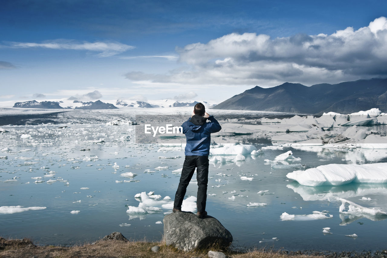 Man standing in front of glaciers against sky