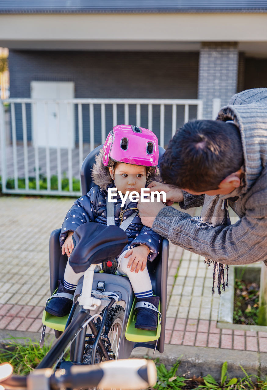 Father adjusting cycling helmet for daughter in park