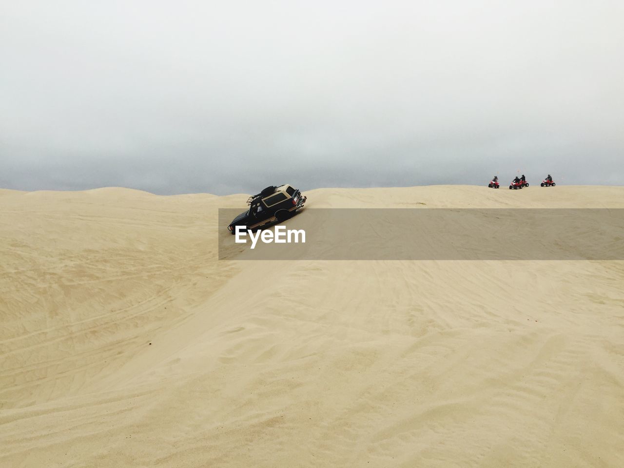 Off-road vehicle on sand dune in desert against sky