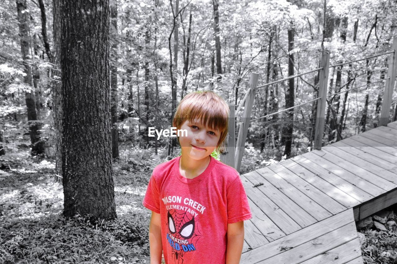 PORTRAIT OF SMILING BOY STANDING ON TREE TRUNK