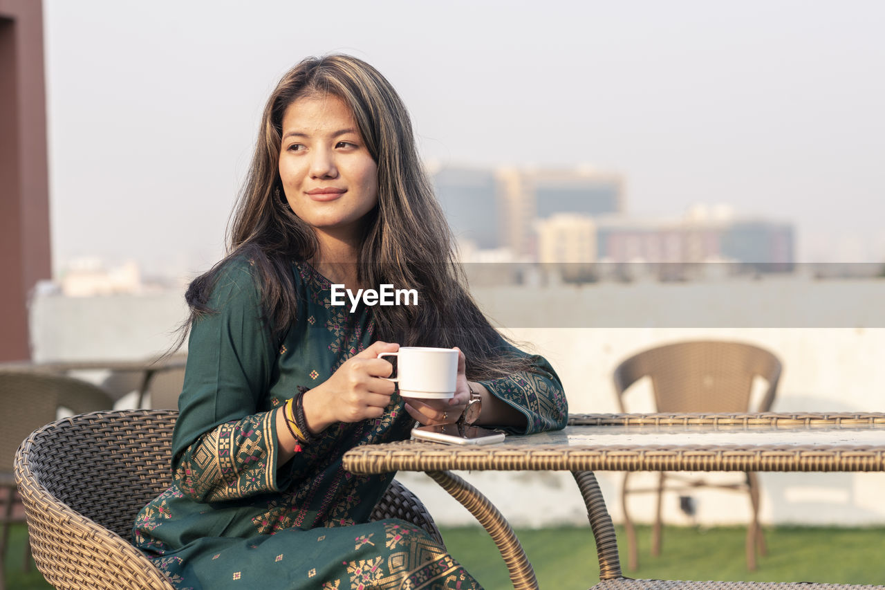 Young indian girl having tea or coffee in a roof top cafe, wearing indian traditional dress.