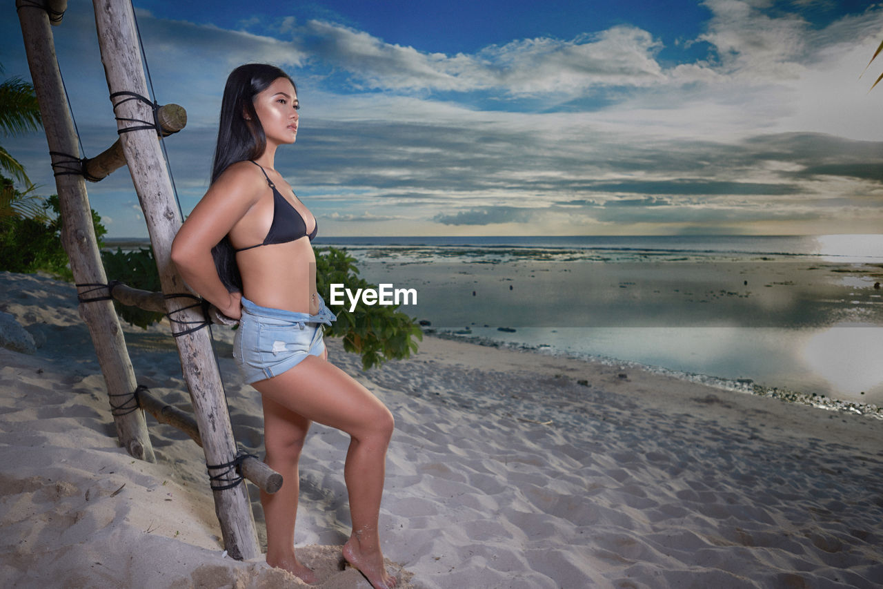 Young woman standing at beach against sky