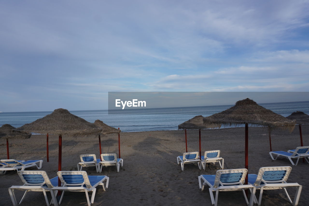 LOUNGE CHAIRS ON BEACH AGAINST SKY
