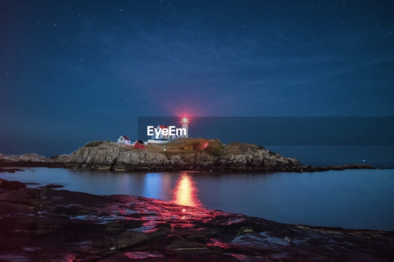 Reflection of illuminated lighthouse in water at night