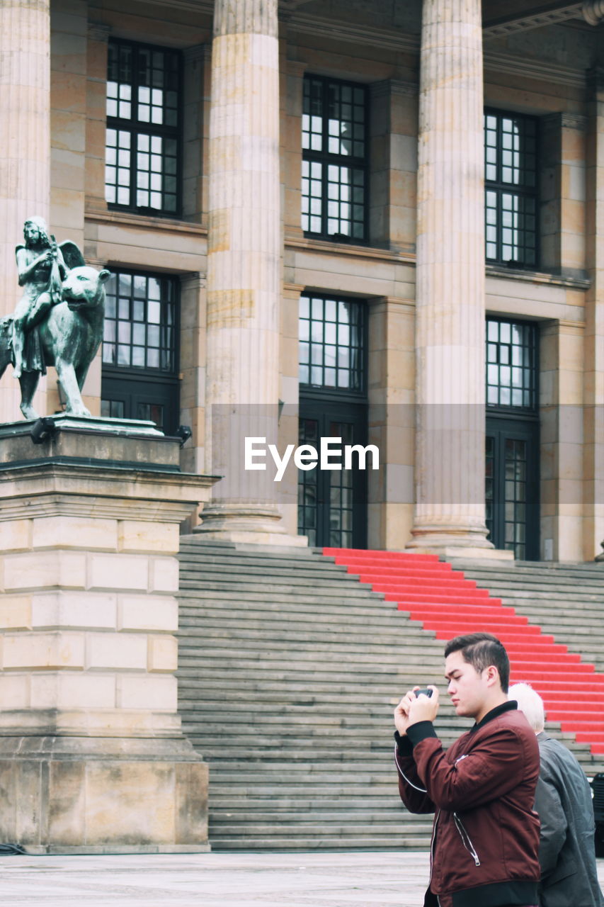 MAN PHOTOGRAPHING WITH STATUE ON BUILDING