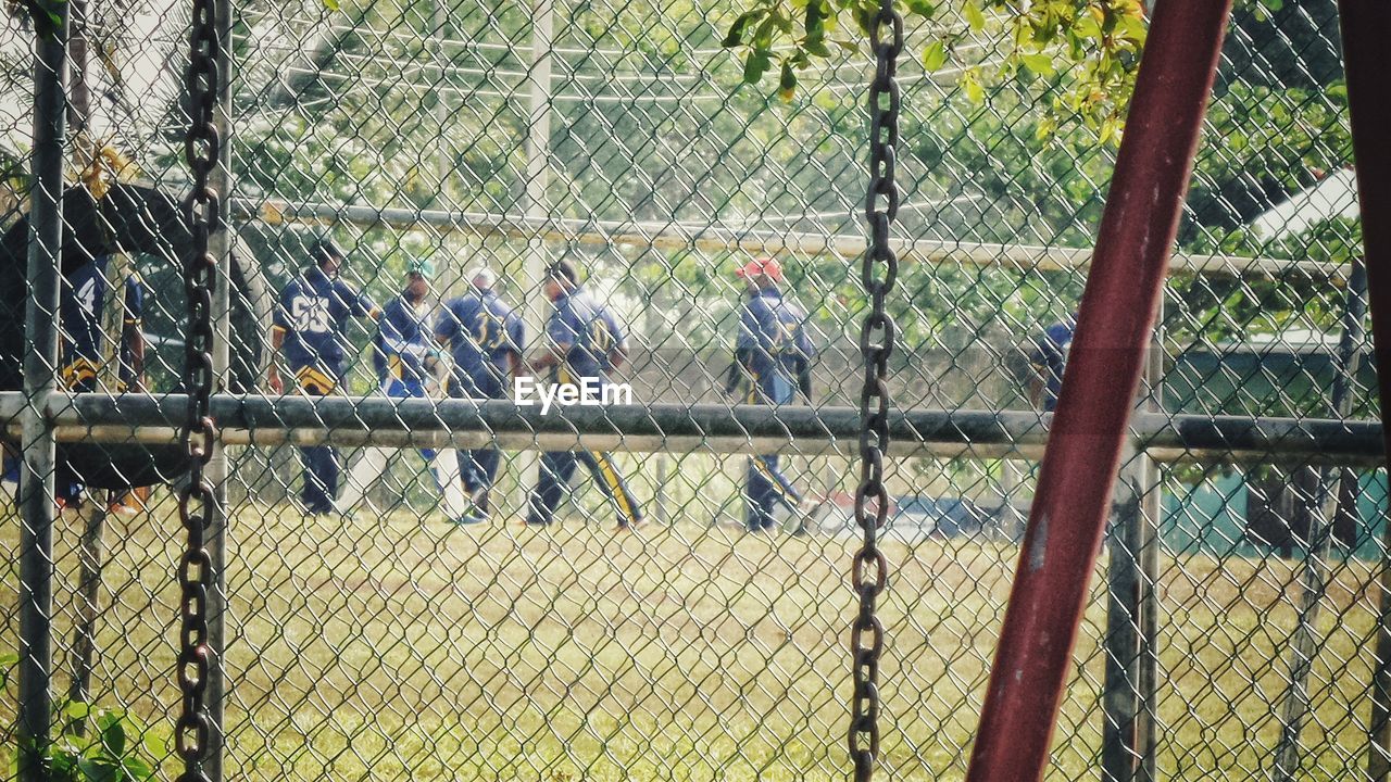 Men playing cricket seen through fence