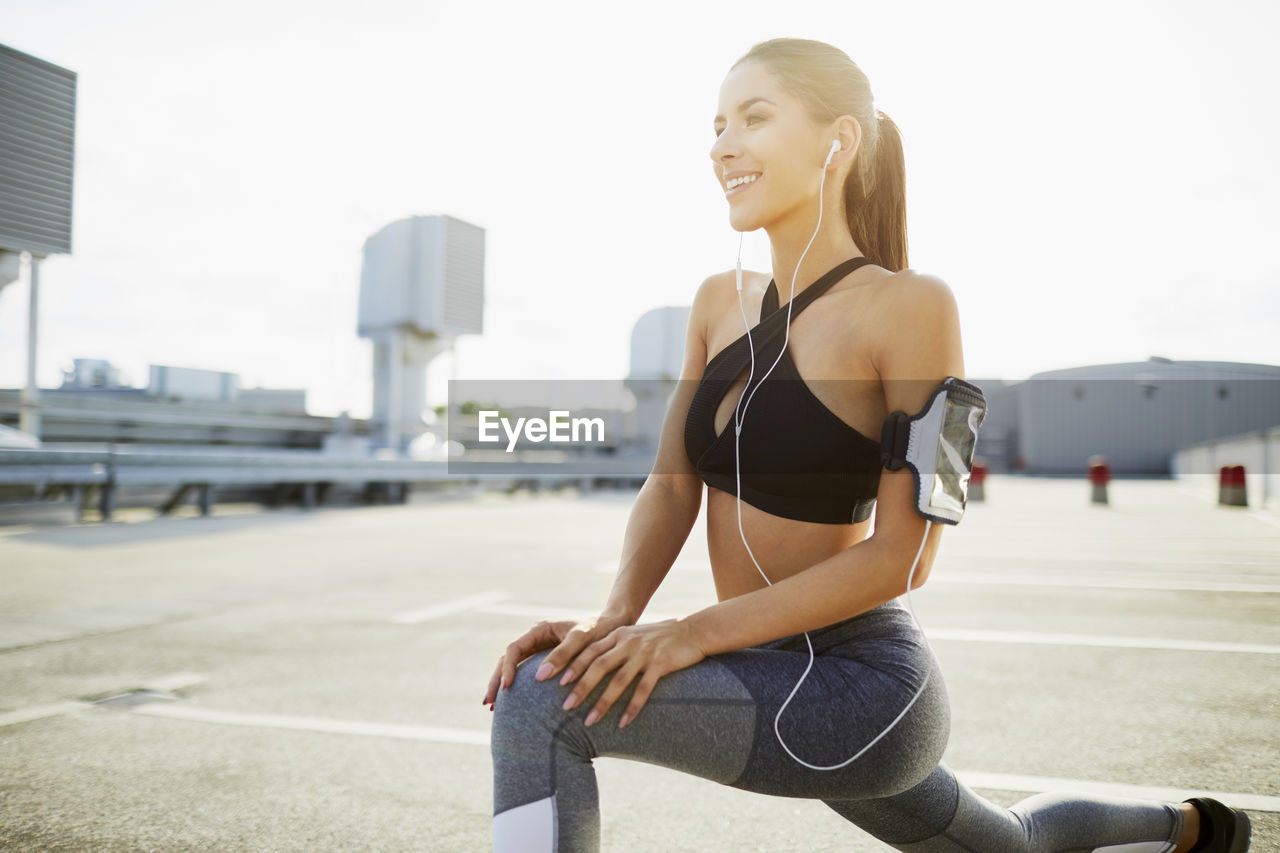 Smiling young woman wearing earphones stretching before jogging