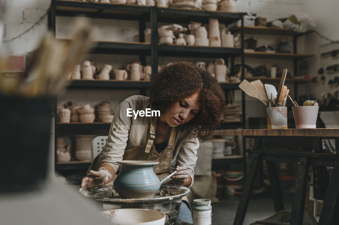 Young potter painting pot on pottery wheel at workshop