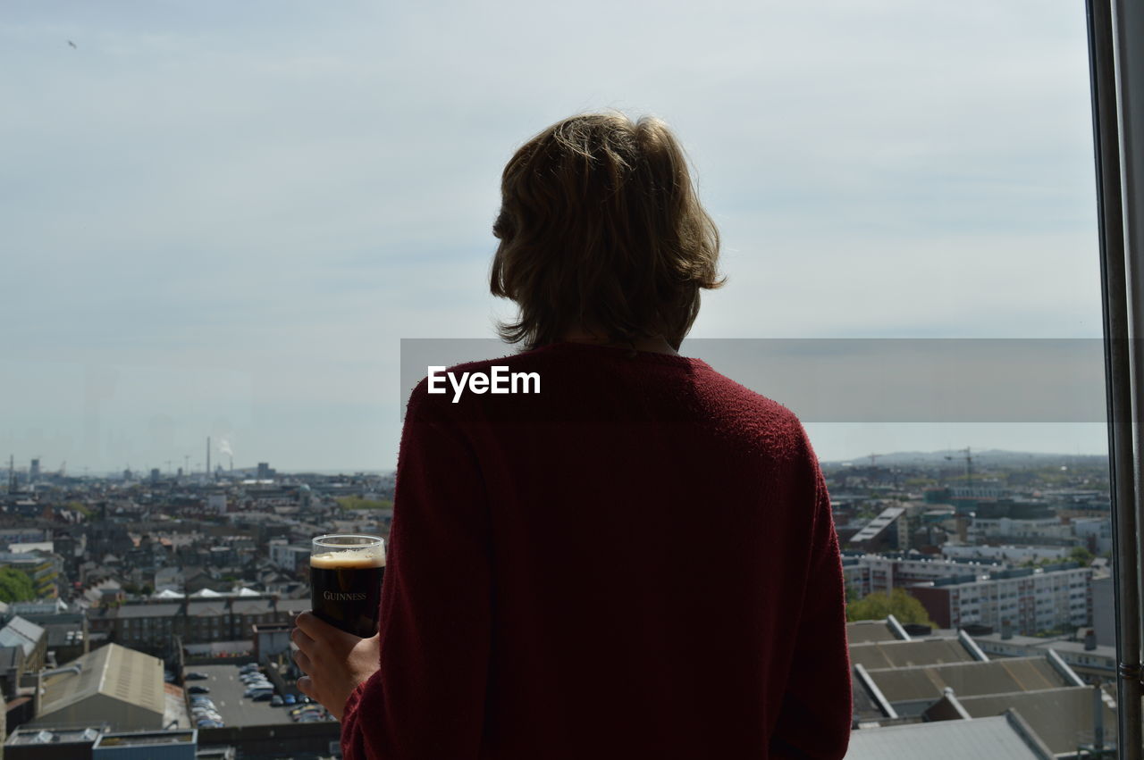 REAR VIEW OF MAN STANDING AGAINST BUILDINGS IN CITY