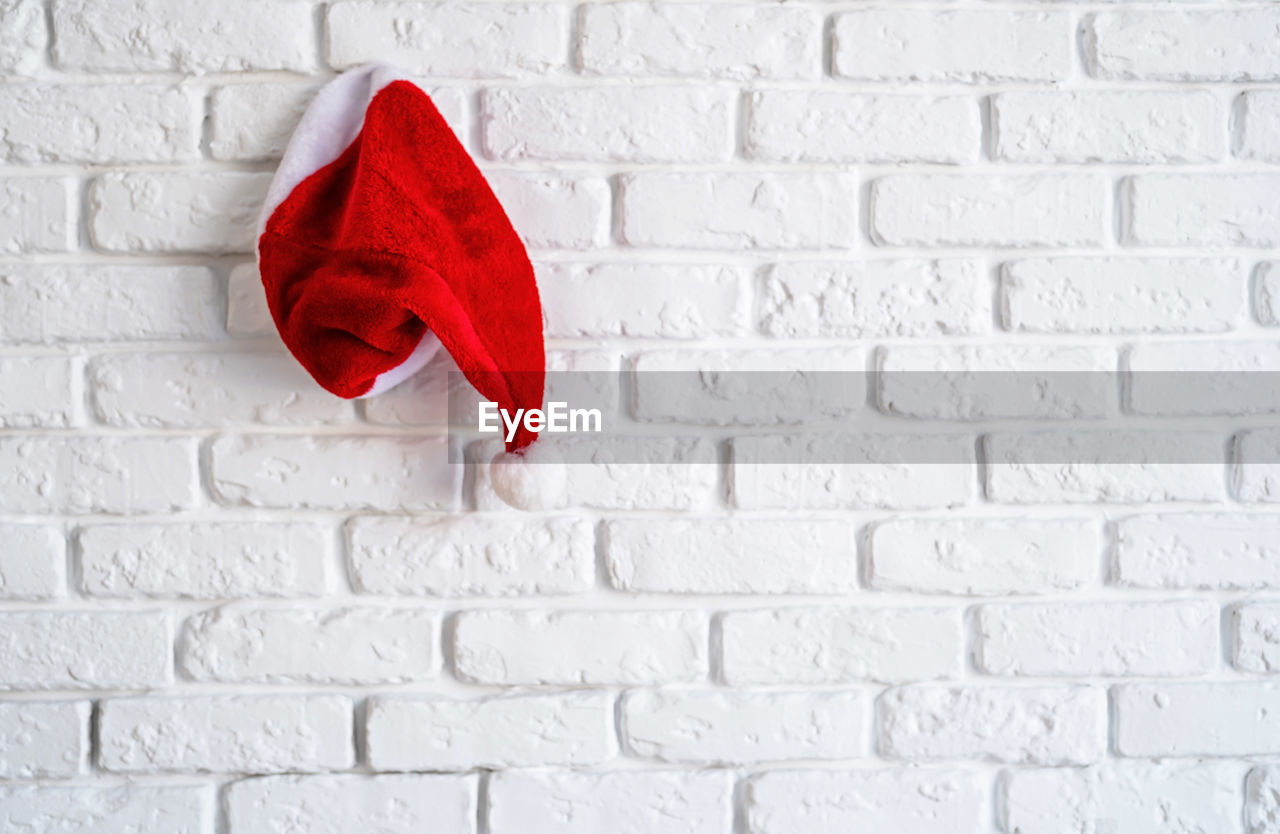 Christmas concept. red santa hat hanging on white bricks wall with copy space