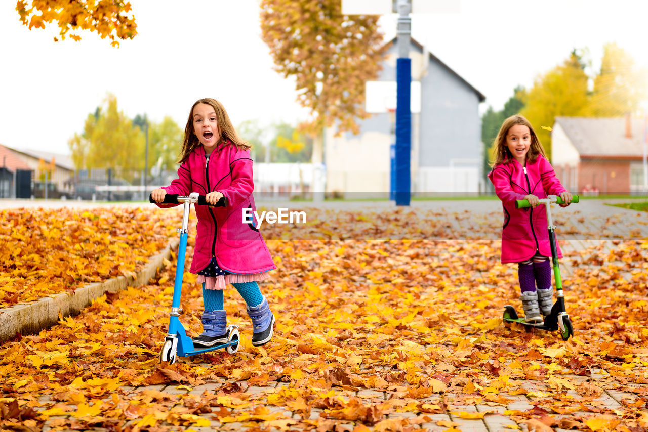 Girls riding push scooters at park during autumn