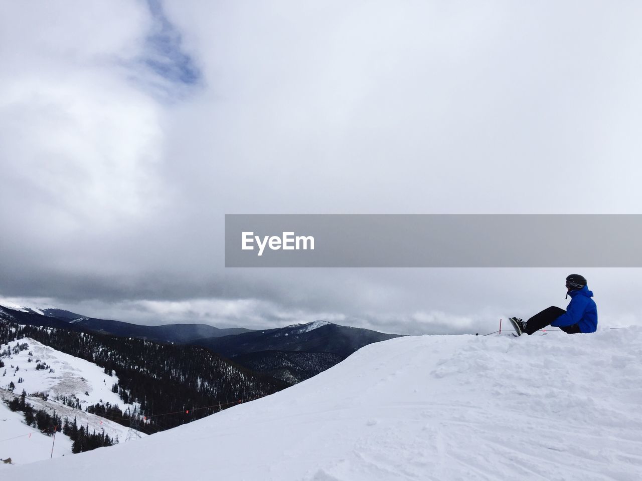 Side view of person sitting on mountain against cloudy sky