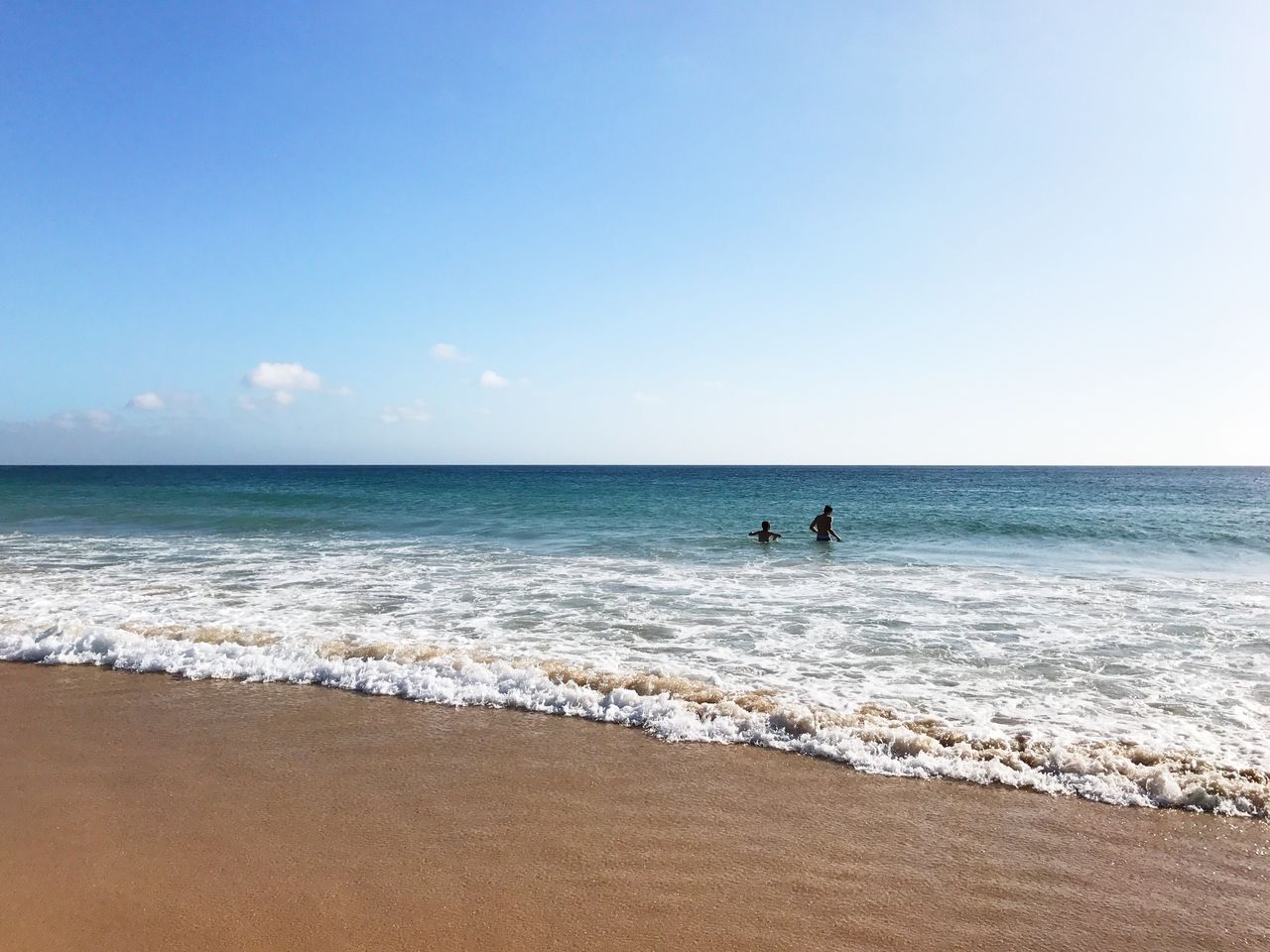 Mid distance view of silhouette people enjoying in sea against sky during sunny day