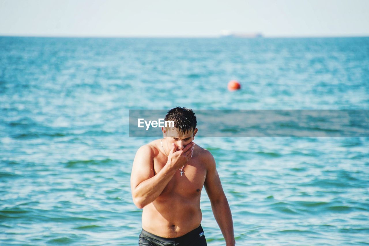 Shirtless man standing in sea against sky