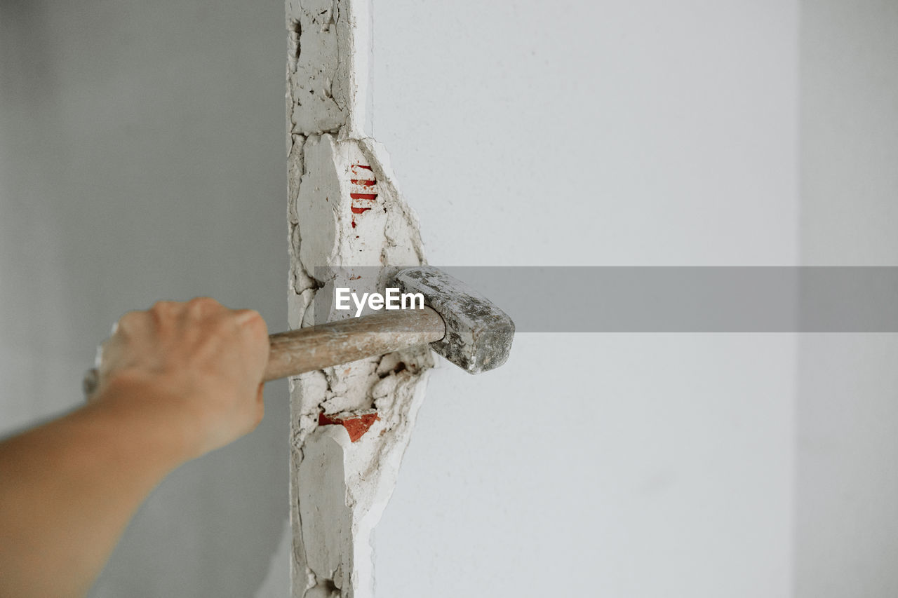 Unrecognizable person holding hammer to demolish wall at construction site. home renovation