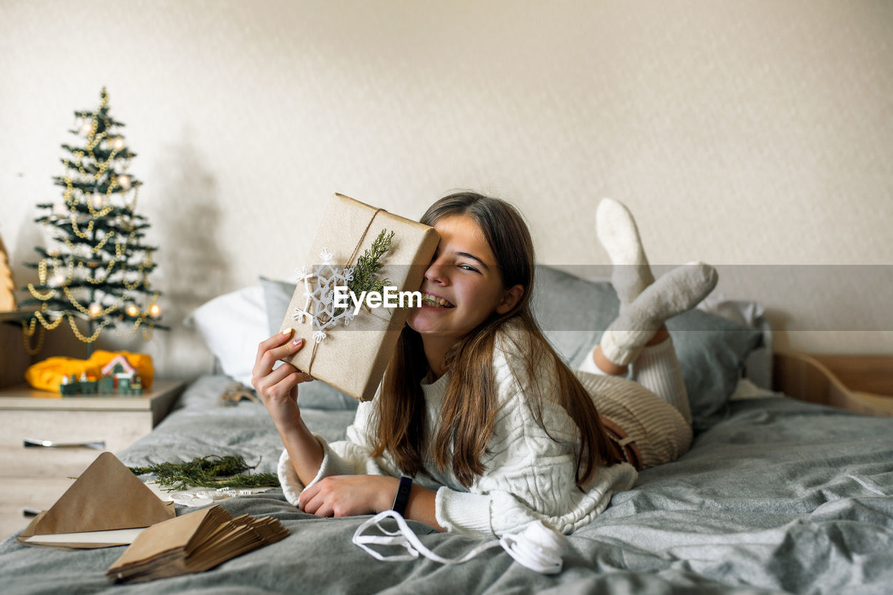 Portrait of smiling girl holding envelope sitting on bed at home