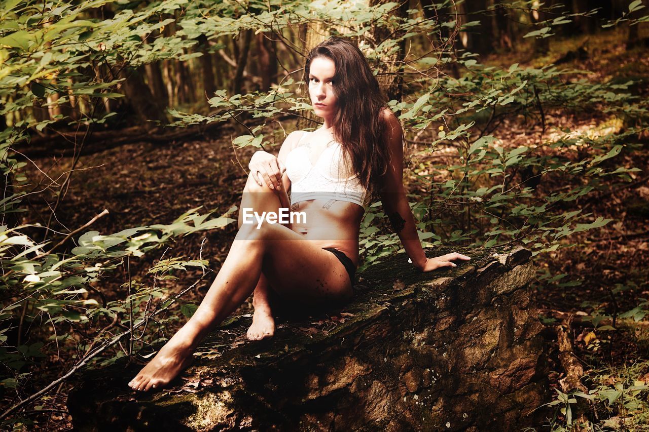 Portrait of young woman sitting on rock in forest