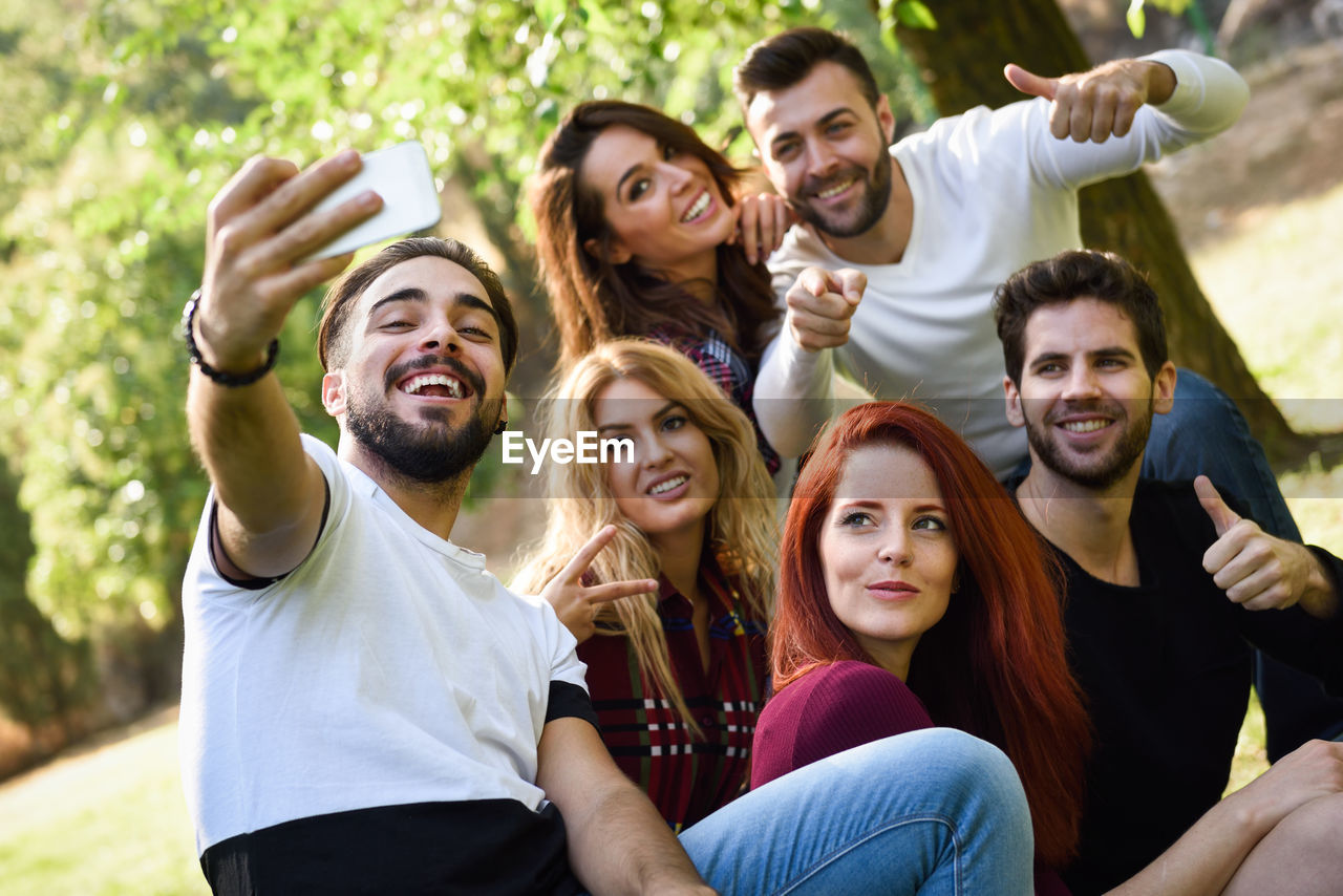 Smiling young man taking selfie with friends at park