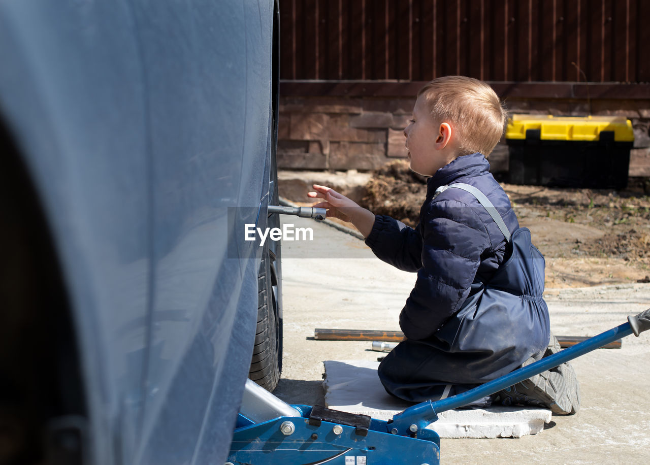 A little boy fixes a car, changes a wheel, helps his dad.