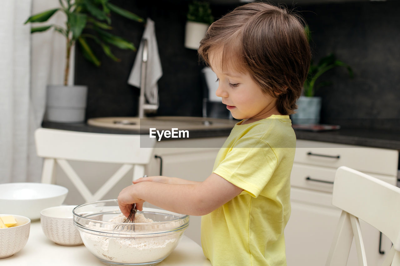 The boy prepares dough for biscuit or baking in the kitchen. the kid mixes the ingredients