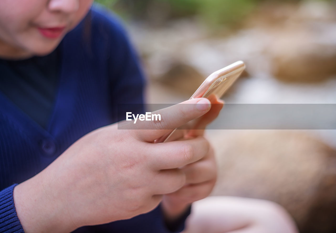 Midsection of woman using smart phone while sitting outdoors