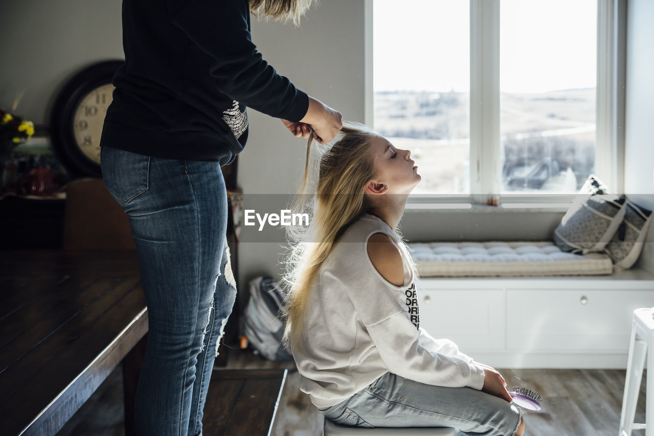 Side view of girl tying sister's hair at home