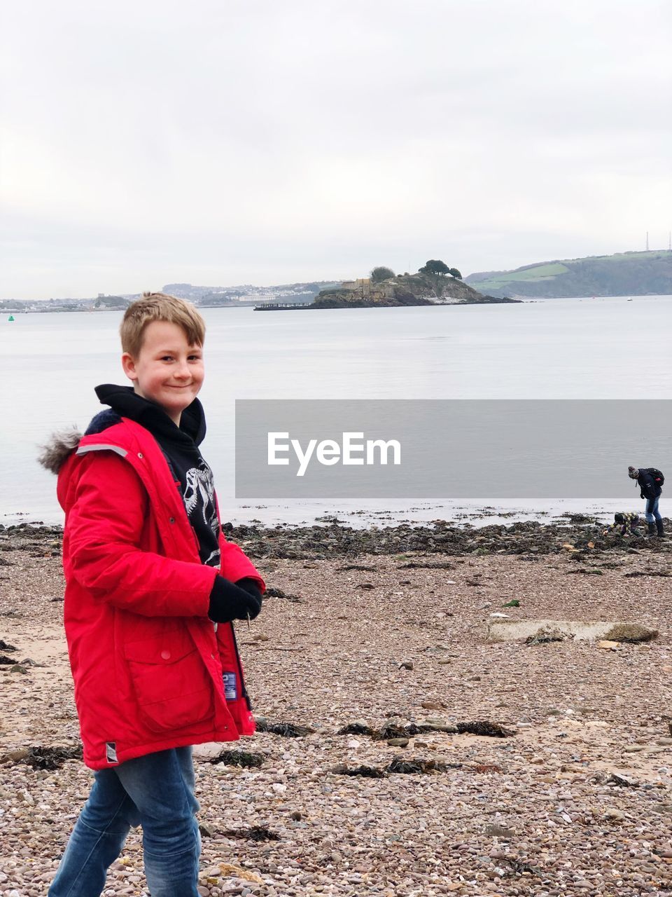 PORTRAIT OF BOY STANDING ON SHORE AGAINST SKY