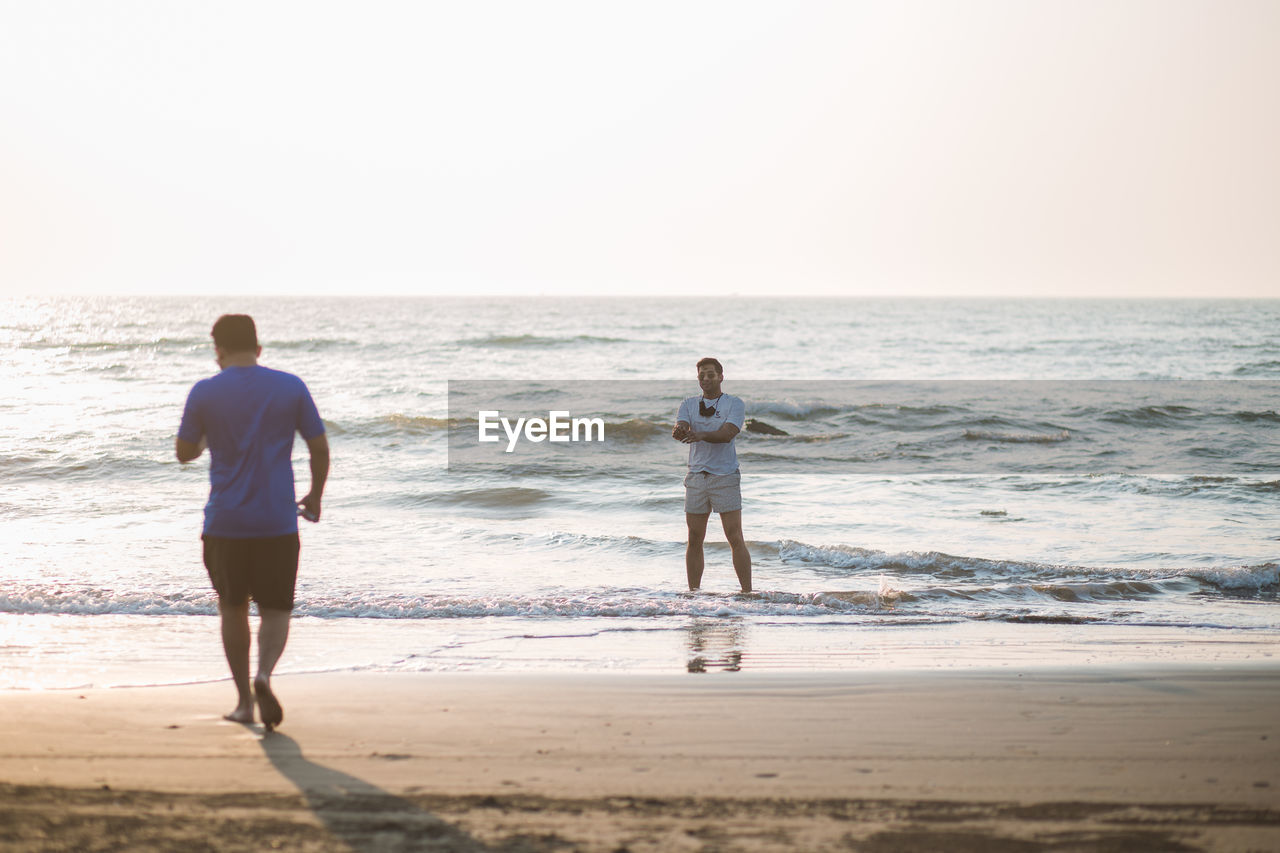 Rear view of man walking on the beach towards another person standing in the water