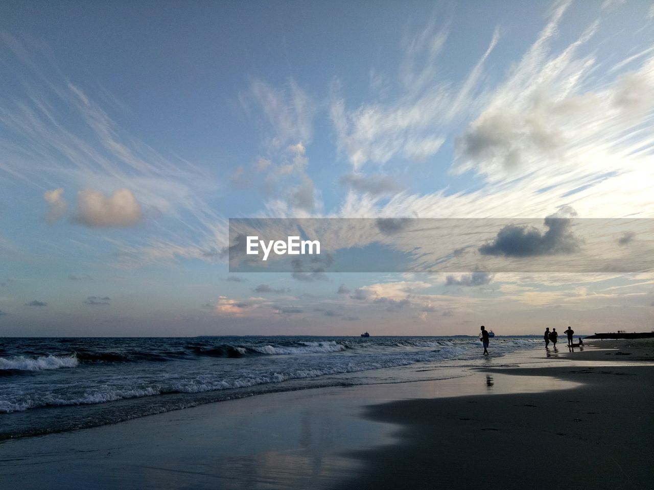 Man walking at beach against sky during sunset