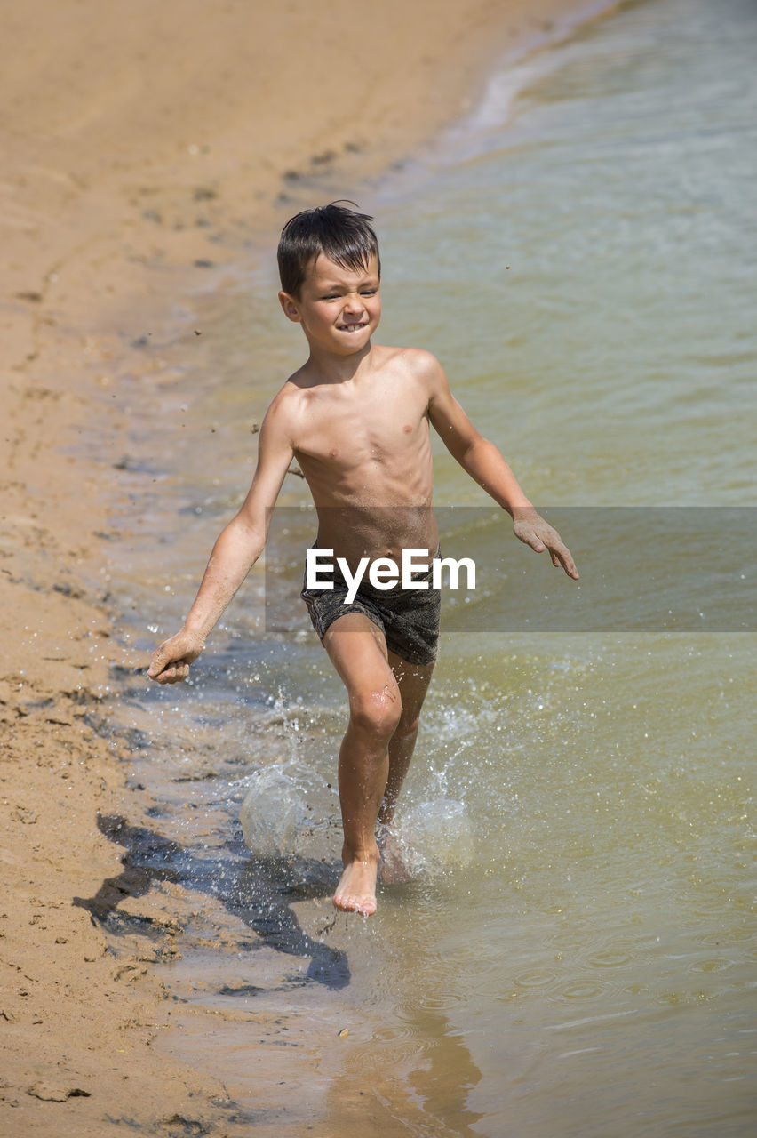 Playful shirtless boy running on shore at beach