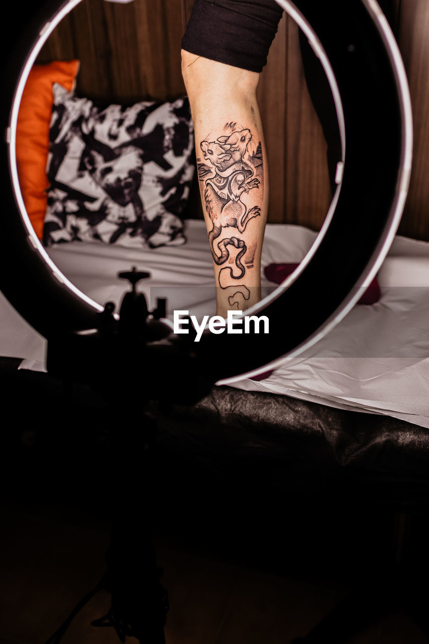 Crop unrecognizable person leg with fresh tattoo in round glowing lamp during photo session in tattoo salon