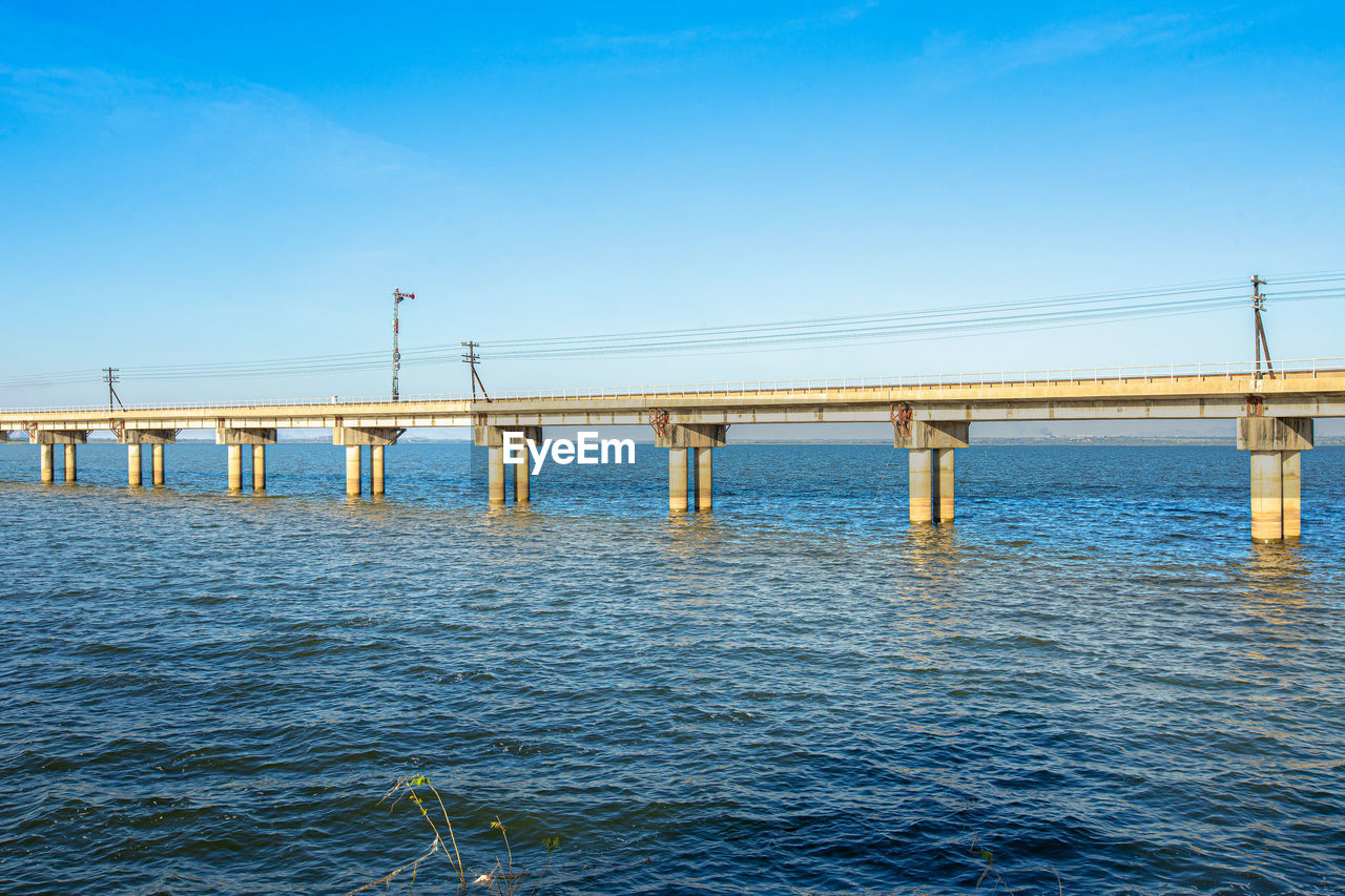 BRIDGE OVER CALM BLUE SEA AGAINST CLEAR SKY