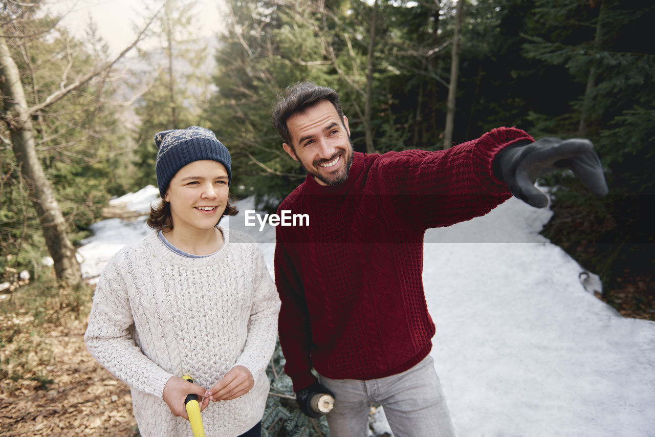 Smiling mature man standing by teenage boy while pointing during winter