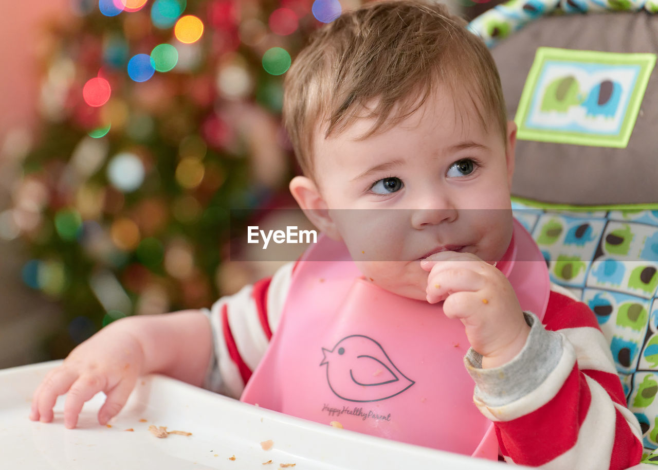 Little boy toddler eating in his high chair in front of the christmas tree