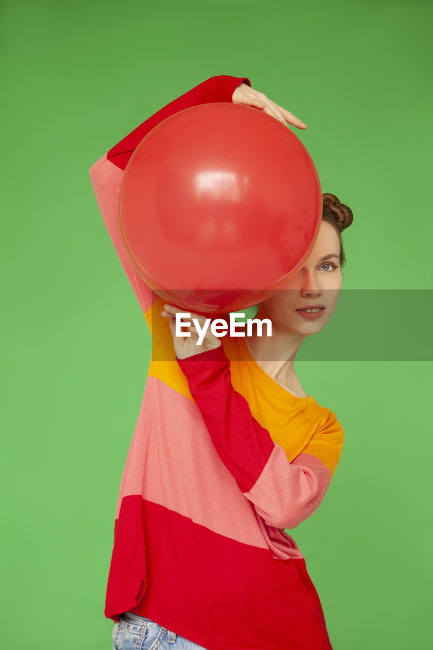Woman with red balloon standing against green background