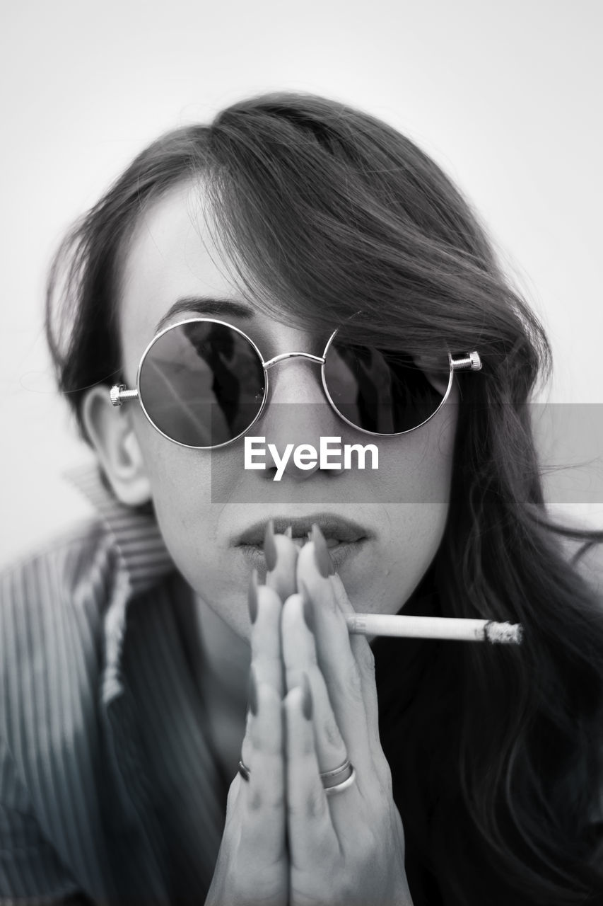 Close-up portrait of confident young woman holding cigarette against white background