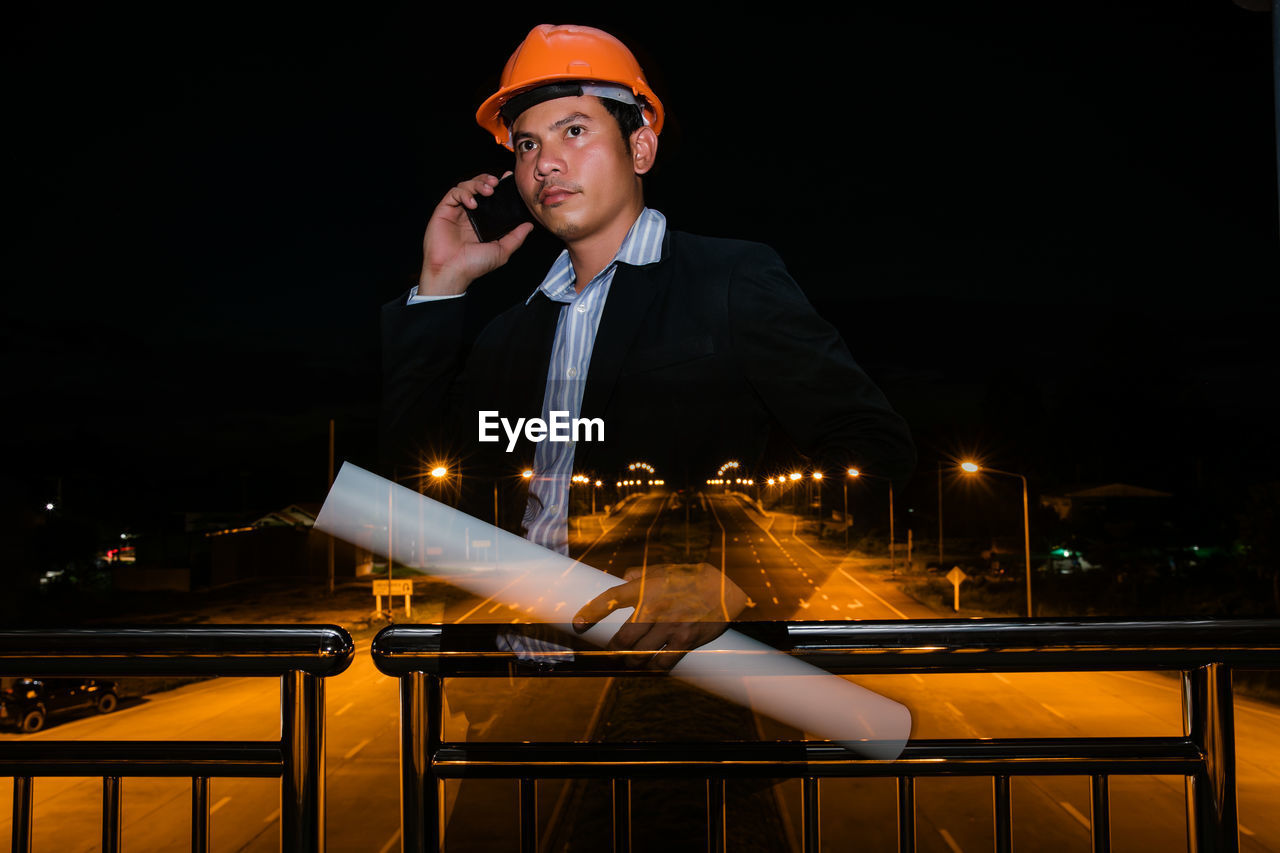 Man talking on phone against railing at night