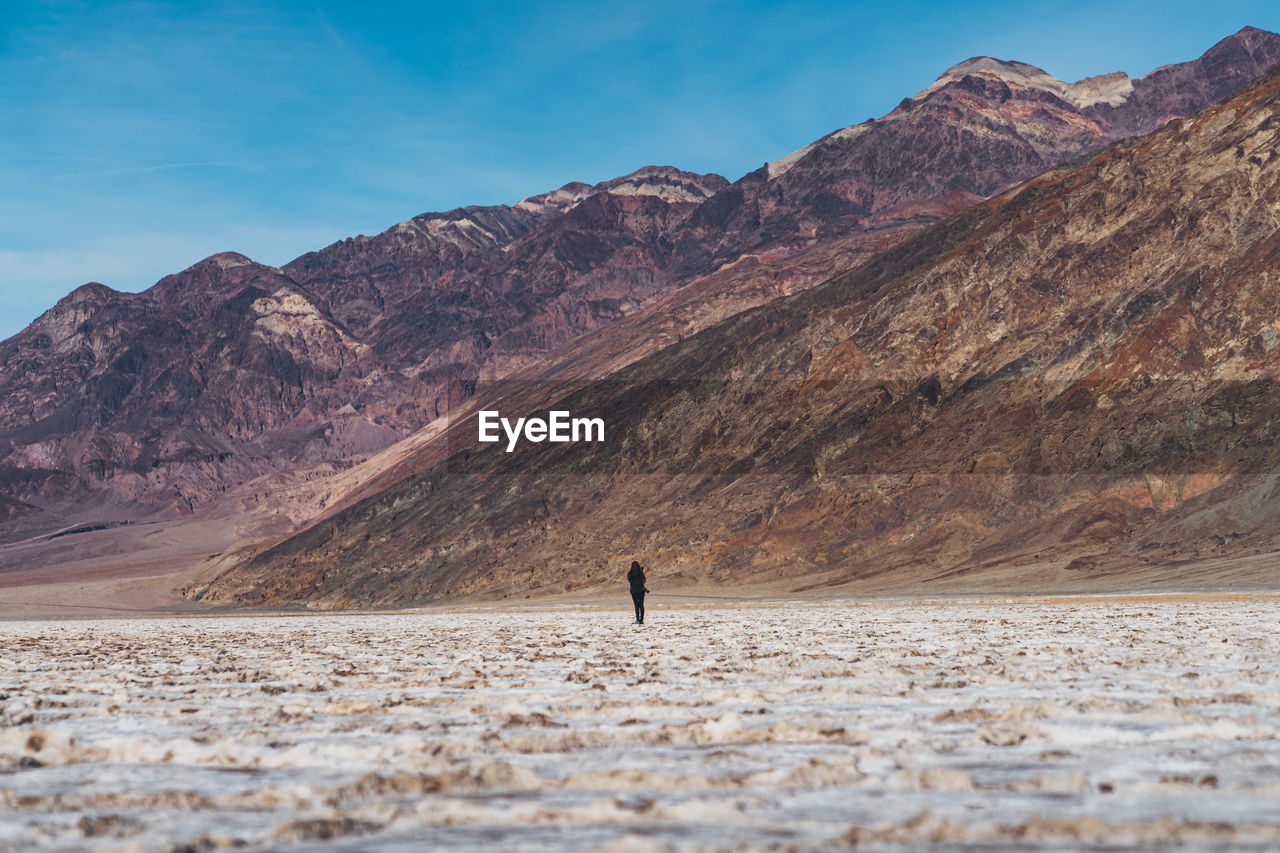 Rear view of woman walking by mountains against sky