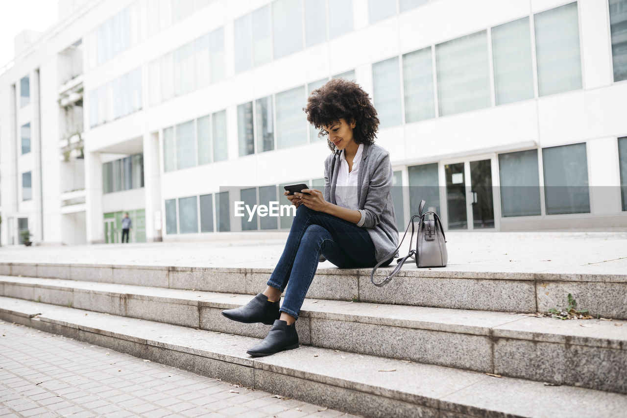 Smiling woman sitting on stairs outdoors using cell phone