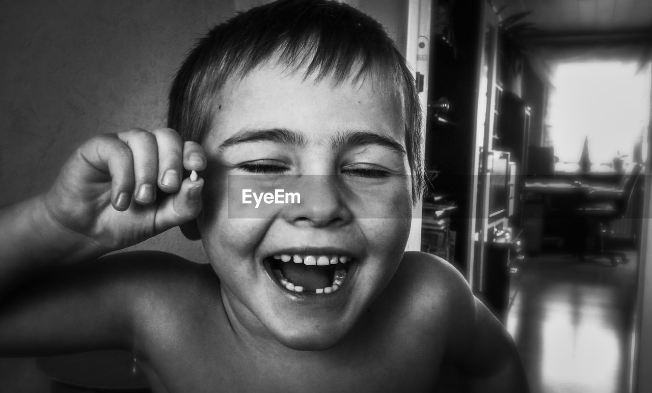 Close-up portrait of laughing shirtless boy who holds his teeth in camera